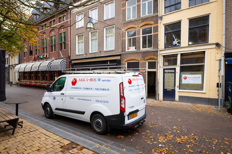 Foto van het witte bedrijfsbusje van Arka Bouw voor een oud pand.